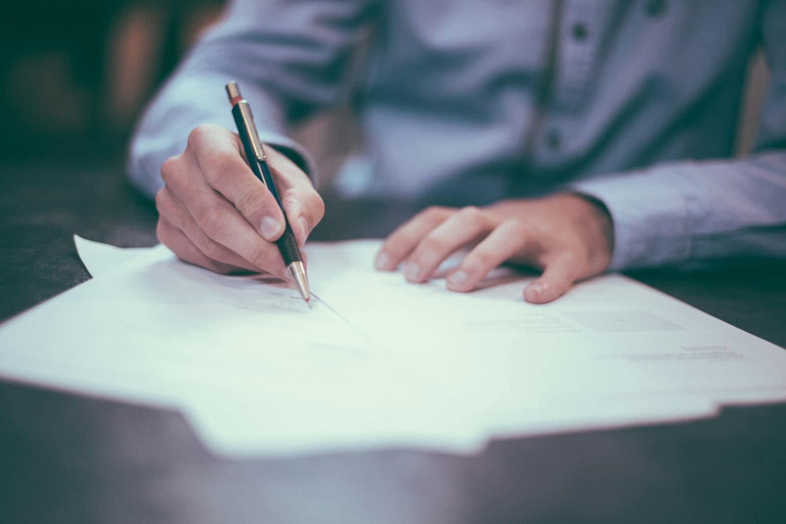 Hands filling out business paperwork on a desk.